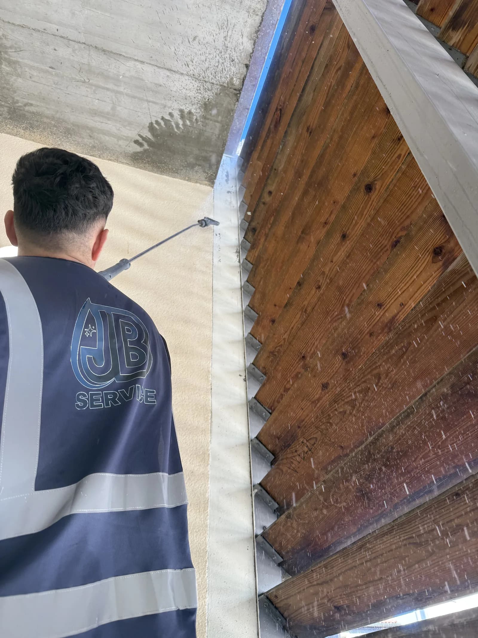 Agent JB Service en gilet floque nettoyant a haute pression la structure bois d'une tribune de gradins a Lyon